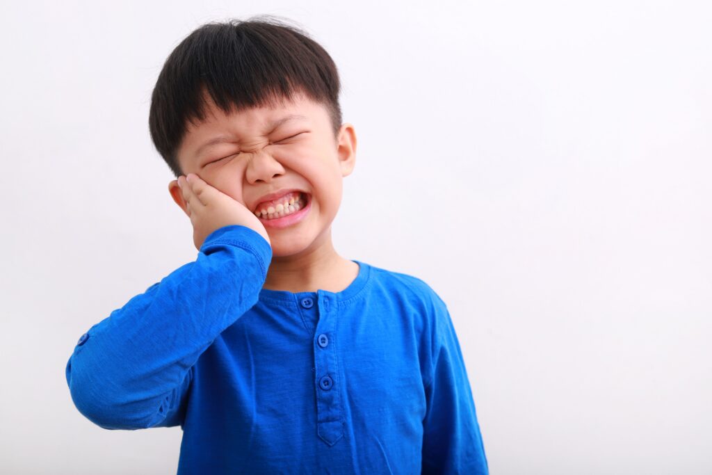 A young boy grimacing in pain, holding his hand to his cheek.