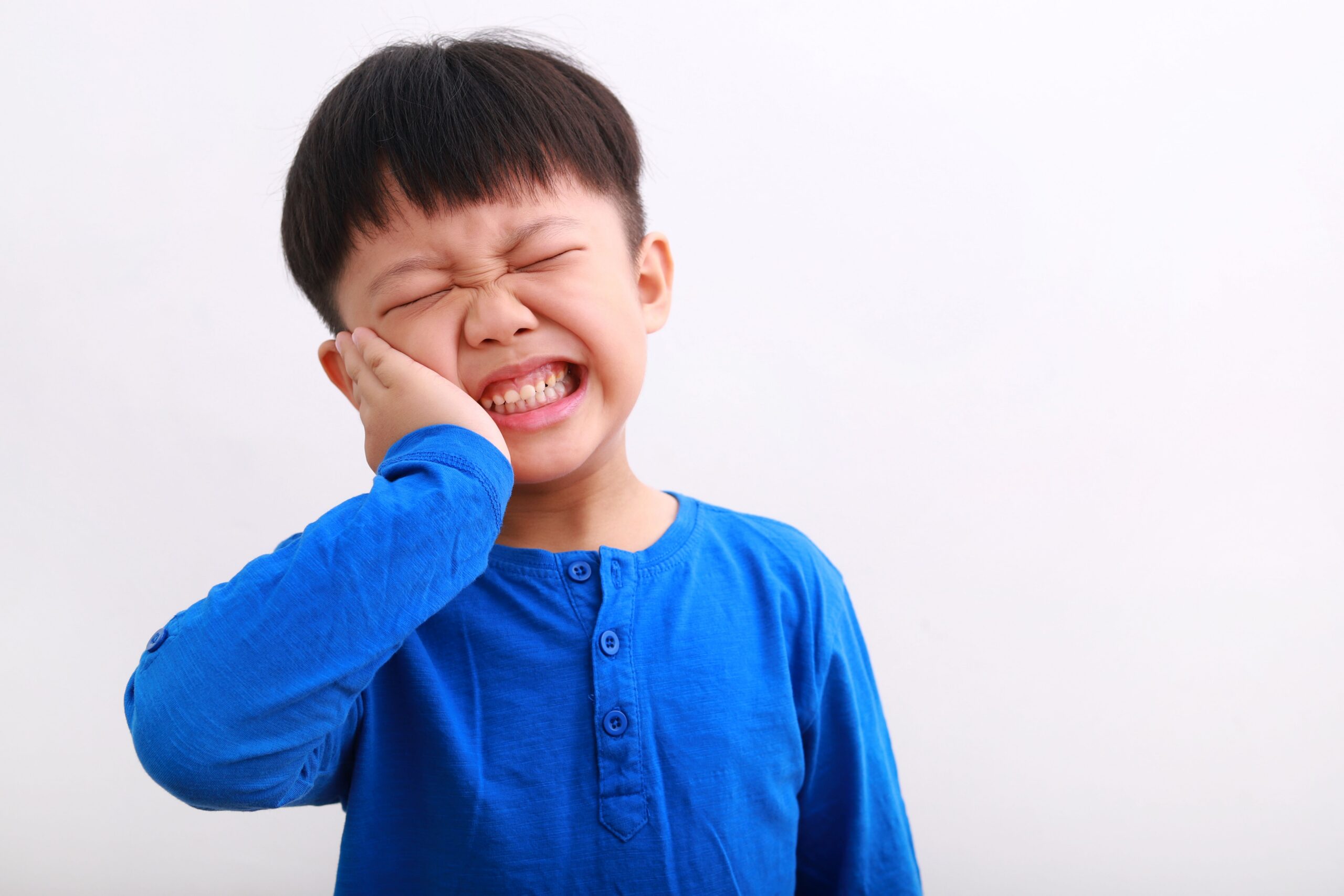 A young boy grimacing in pain, holding his hand to his cheek.