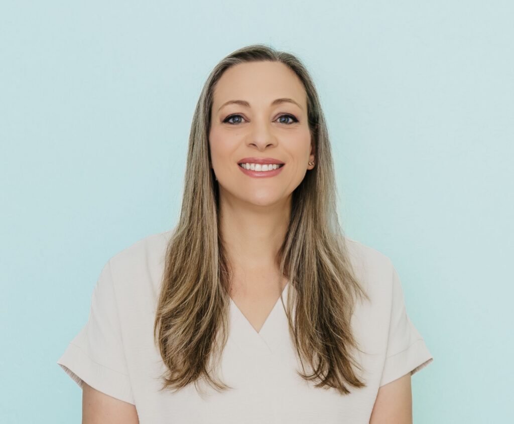 Smiling woman with long blonde and gray hair against a light blue background.